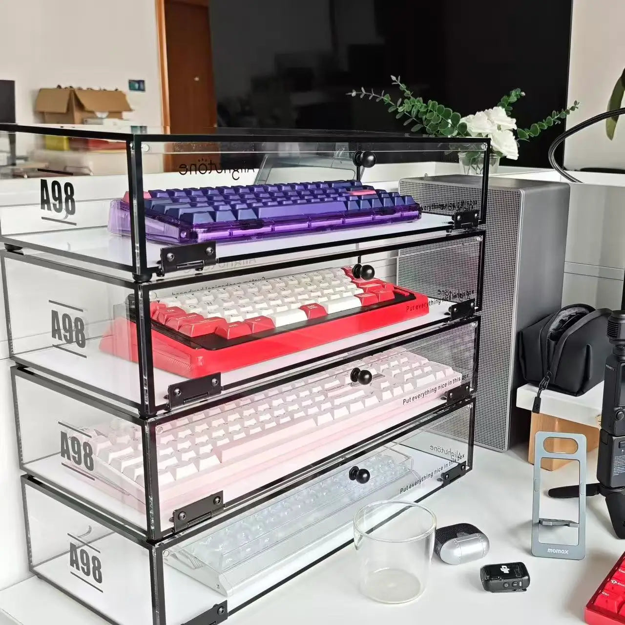 Stackable keyboard organizer stand with four transparent shelves holding keyboards, black frame