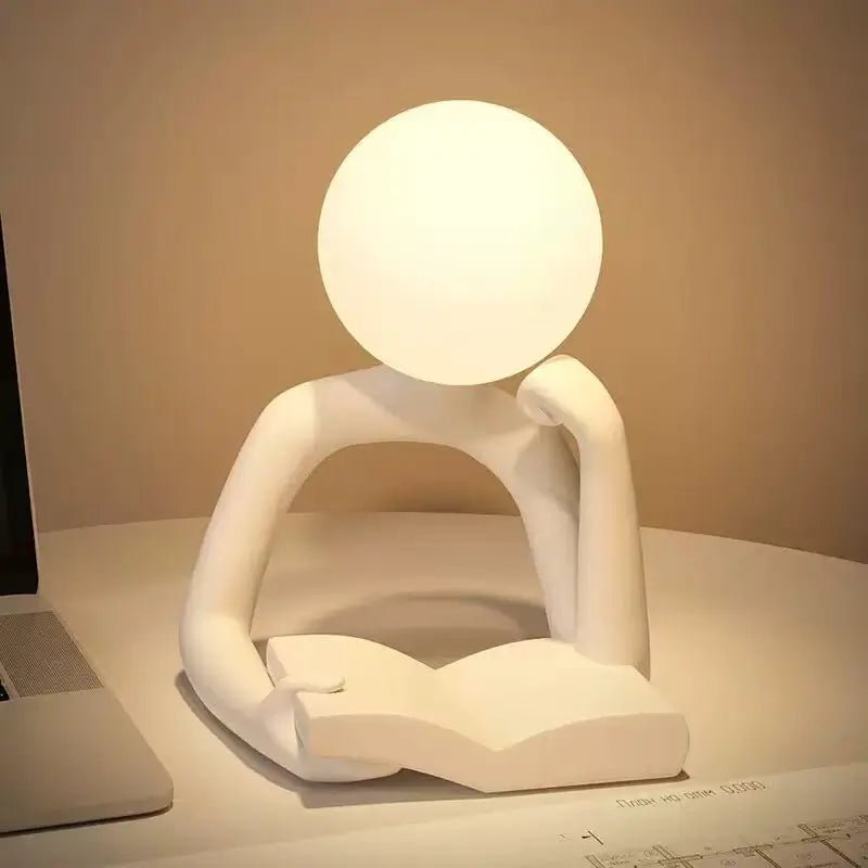 White thinker figure table lamp with glowing round head and seated pose