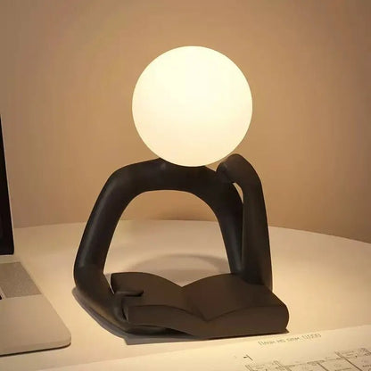 Black thinker figure table lamp with glowing round head, hands resting on base